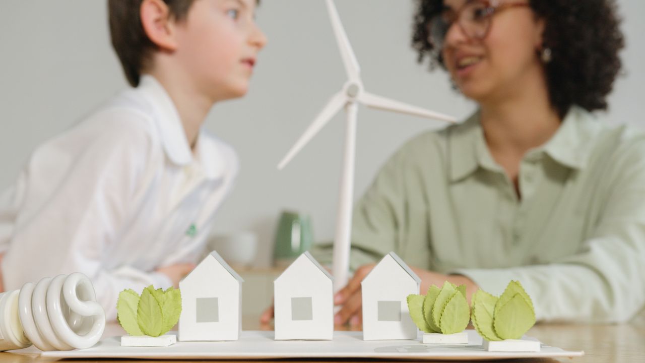 about-me-img Children engage in learning about renewable energy with wind turbines and eco-friendly models in a classroom setting.