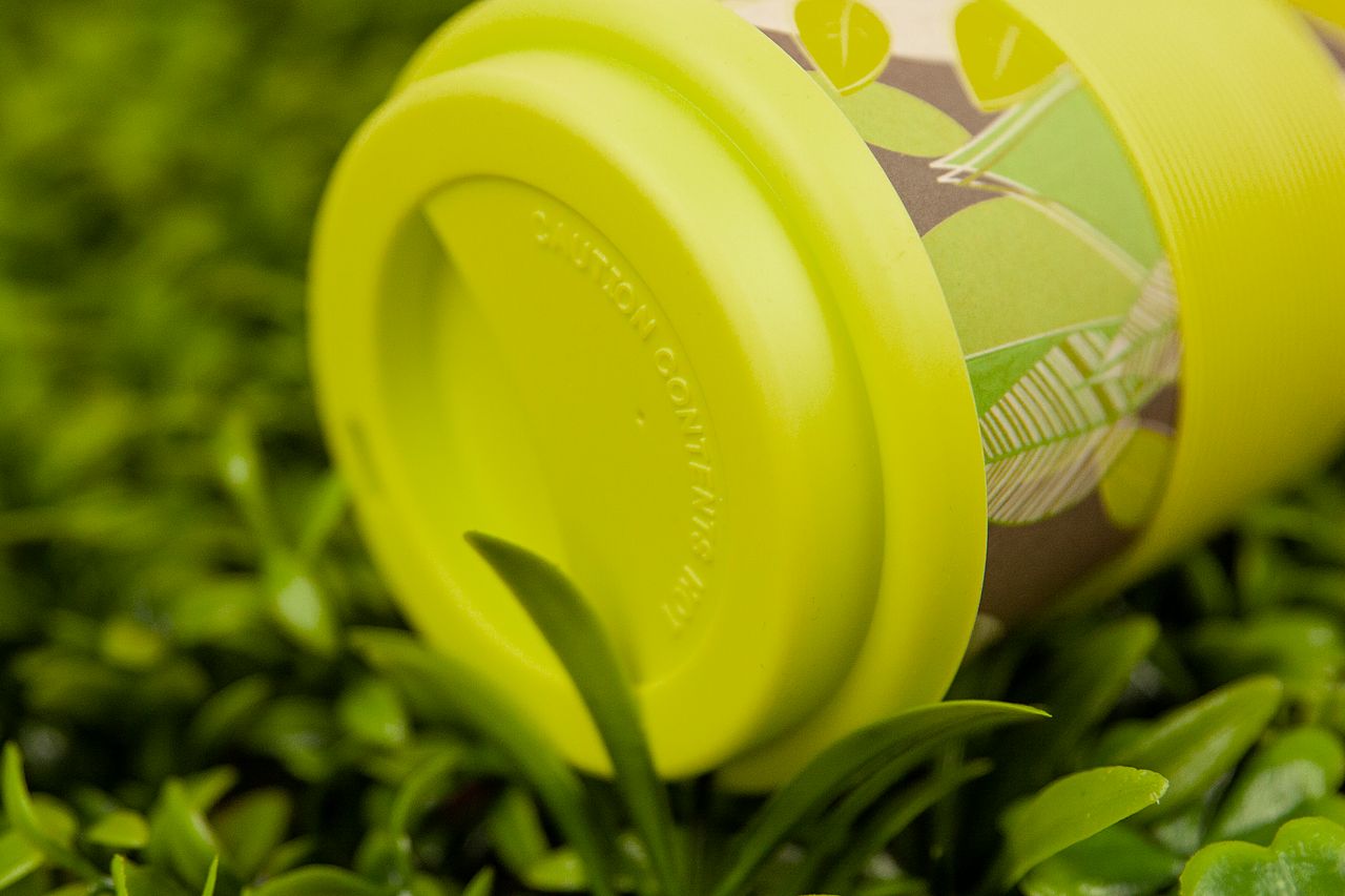 Close-up of a vibrant yellow reusable cup resting on green grass, emphasizing eco-friendly living.